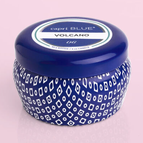 blue candle tin labeled capri blue volcano scent on a light pink background