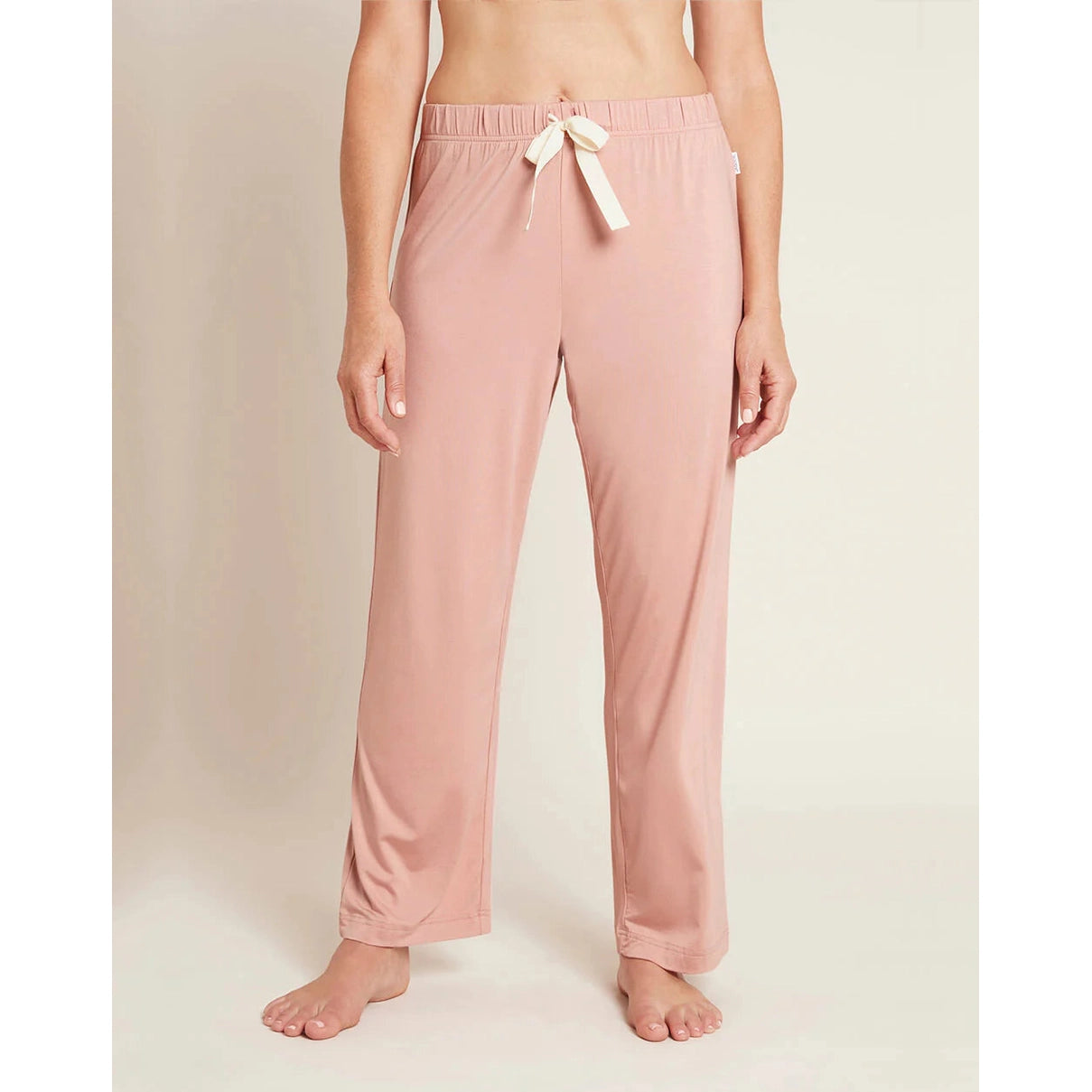 A person standing wearing pink sleep pants with a drawstring and a wide leg design.