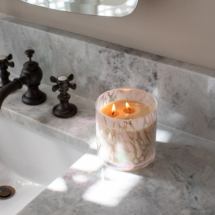 Photo of a burning candle with an white  tortoise finish, containing a white wax, housed in a clear glass vessel.