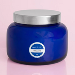 A blue glass jar candle with a silver lid, labeled 'VOLCANO', on a pink background.