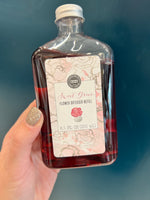 A bottle of Sweet Grace Flower Diffuser Oil Refill with a label in front, on a blue background