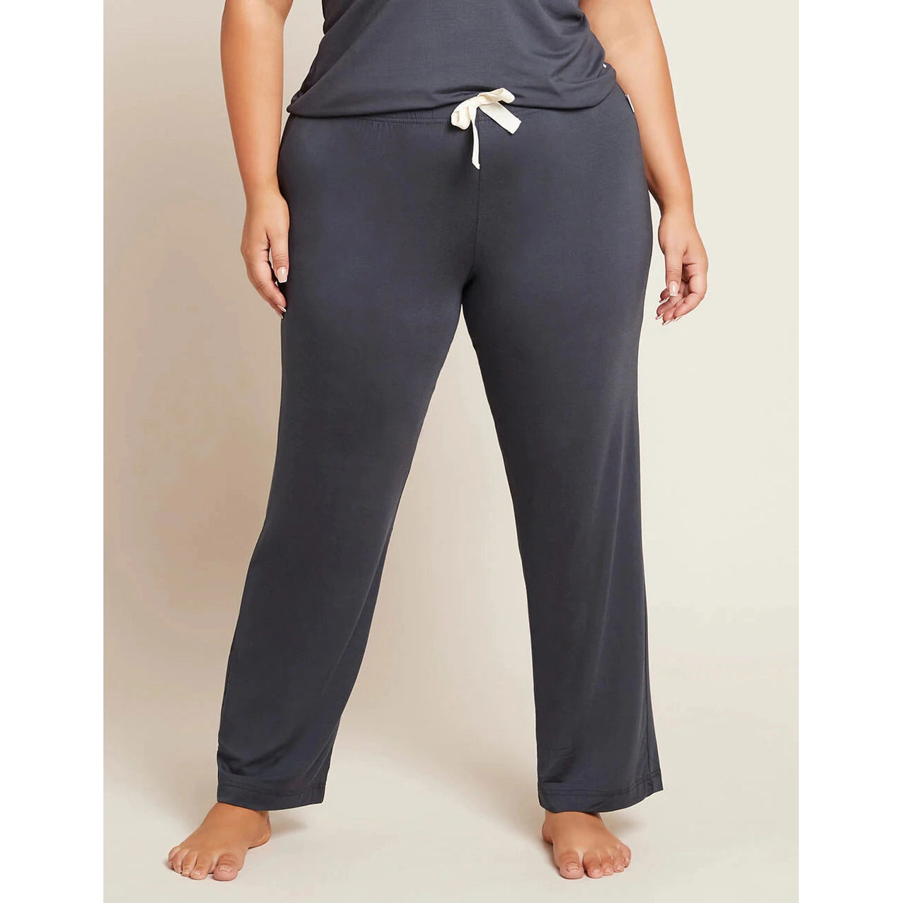 A person standing wearing grey 
sleep pants with a drawstring and a wide leg design.