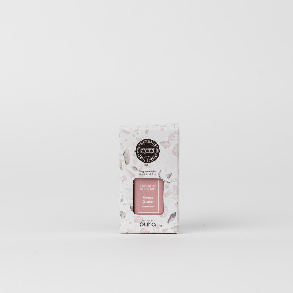 A PURA branded fragrance diffuser vial in a pink shade, placed in front of a white background, with the product packaging behind it.